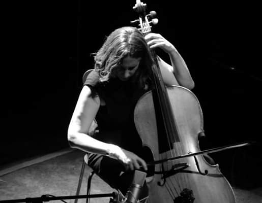 Long haired musician playing a cello on stage. Photo is black and white.