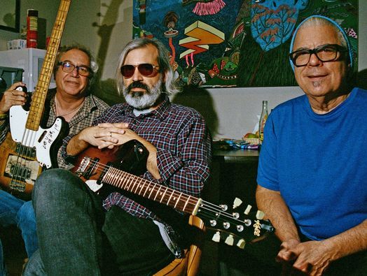 what is assumed to be the band mssv, a trio, sitting and looking at the camera holding their instruments.